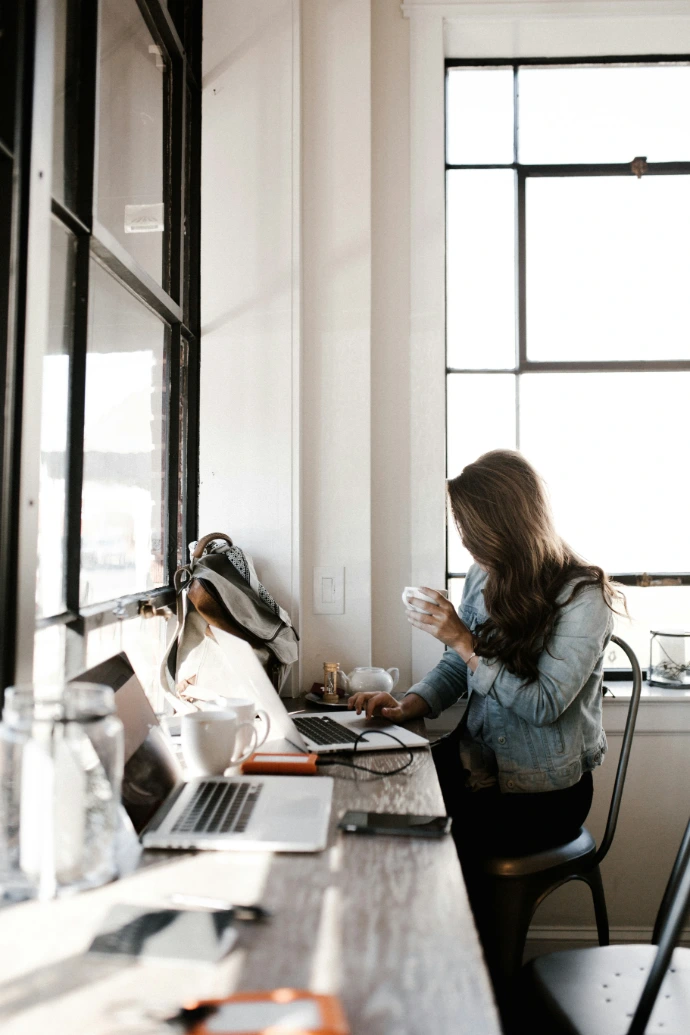 Dirigeante suivant la comptabilité de son entreprise sur son ordinateur portable, tasse de café à la main