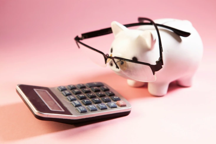 Tirelire avec des lunettes devant une calculatrice, symbole du suivi de la TVA et de la trésorerie de l'entreprise