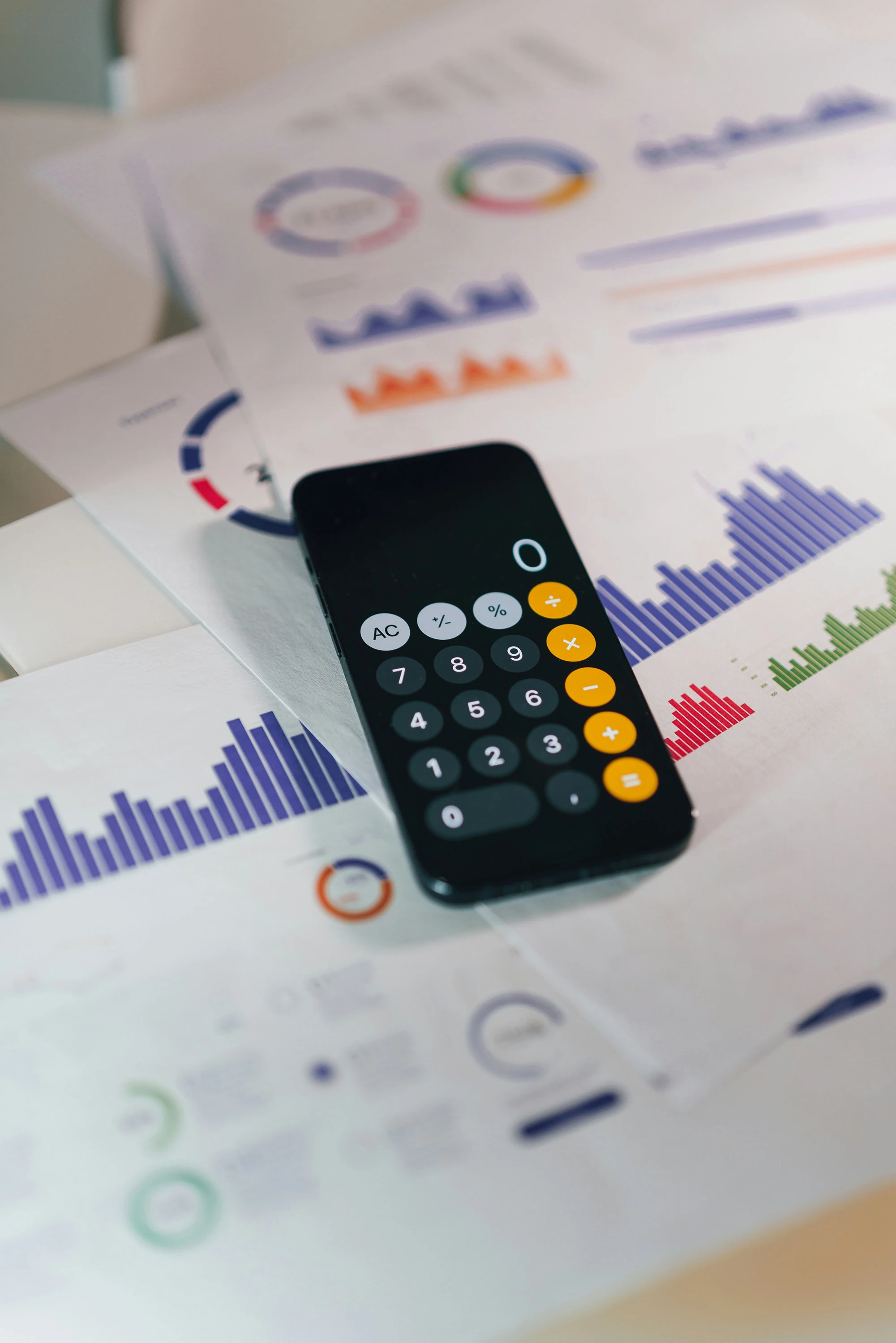 Smartphone en mode calculatrice posé sur des rapports chiffrés et graphiques, analyse du bilan d'une entreprise